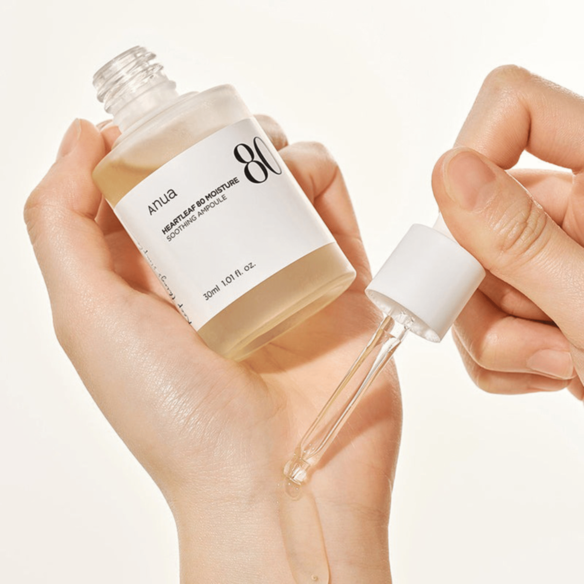 Eine Hand hält eine geöffnete Flasche Anua Heartleaf 80% Soothing Ampoule 30ml, während eine Pipette die Flüssigkeit auf den Rücken einer anderen Hand tropft.