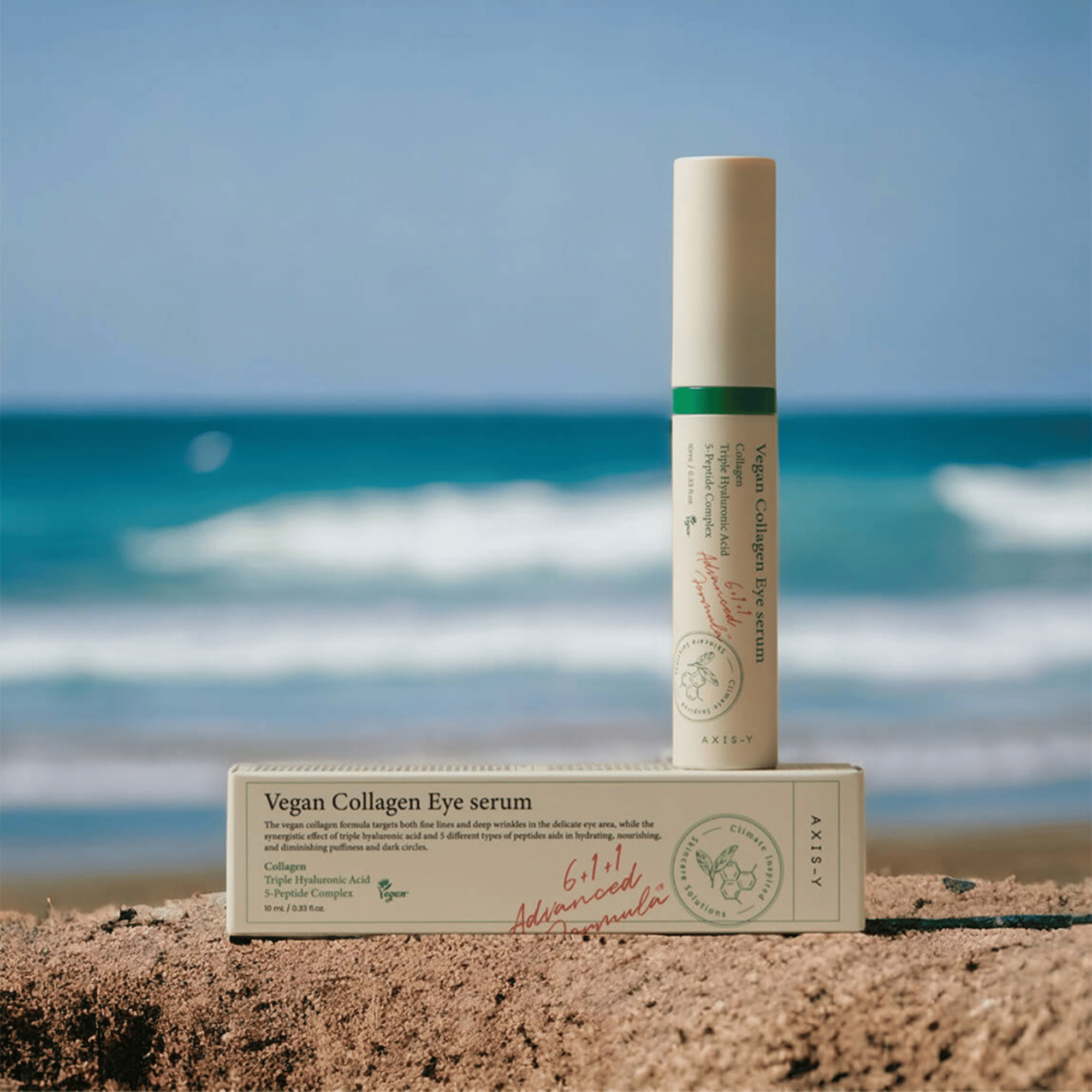 AXIS-Y Vegan Collagen Eye Serum stehend im Sand vor unscharfem Meereshintergrund, neben Umverpackung