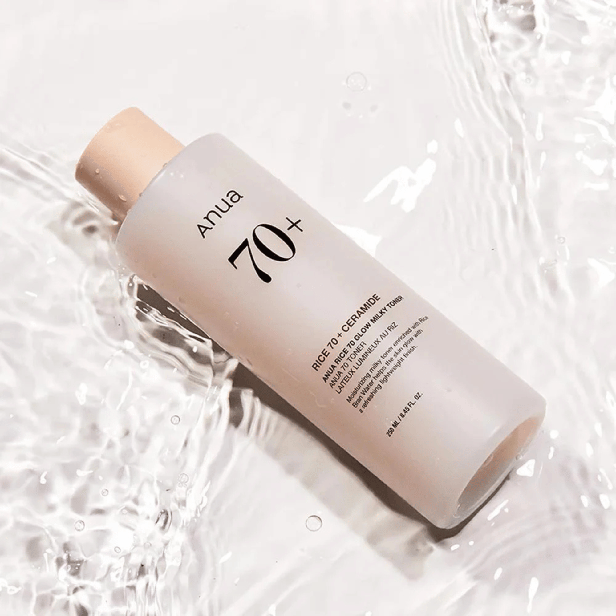 Anua Rice 70+ Glow Milky Toner auf glasklarem Wasser liegend – sanfte Lichtreflexe betonen die cremige Textur
