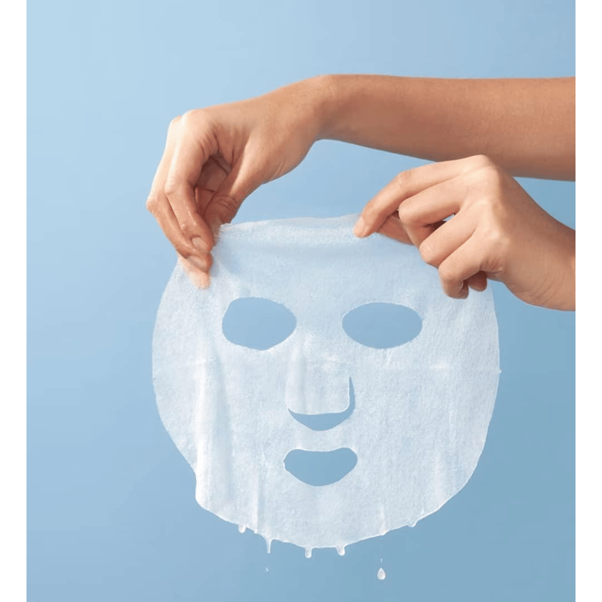 Eine Person hält vor einem schlichten blauen Hintergrund eine Dr. Jart+ Vital Hydra Solution-Maske mit Löchern für Augen, Nase und Mund hoch.