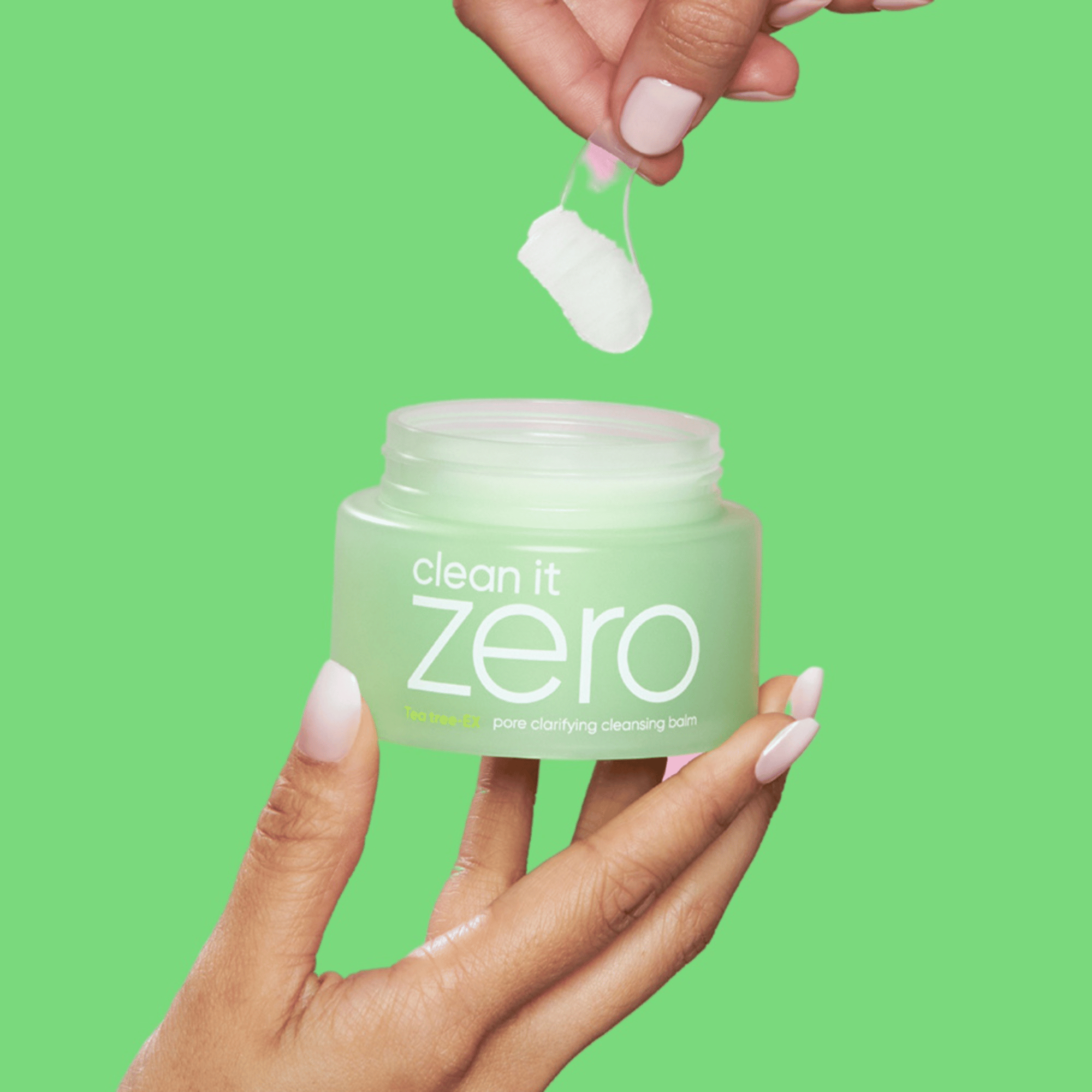 Geöffneter Tiegel des Banila CO Clean It Zero Pore Clarifying Cleansing Balm in der Hand, mit grünem Hintergrund und Spatel, der den Balsam entnimmt.