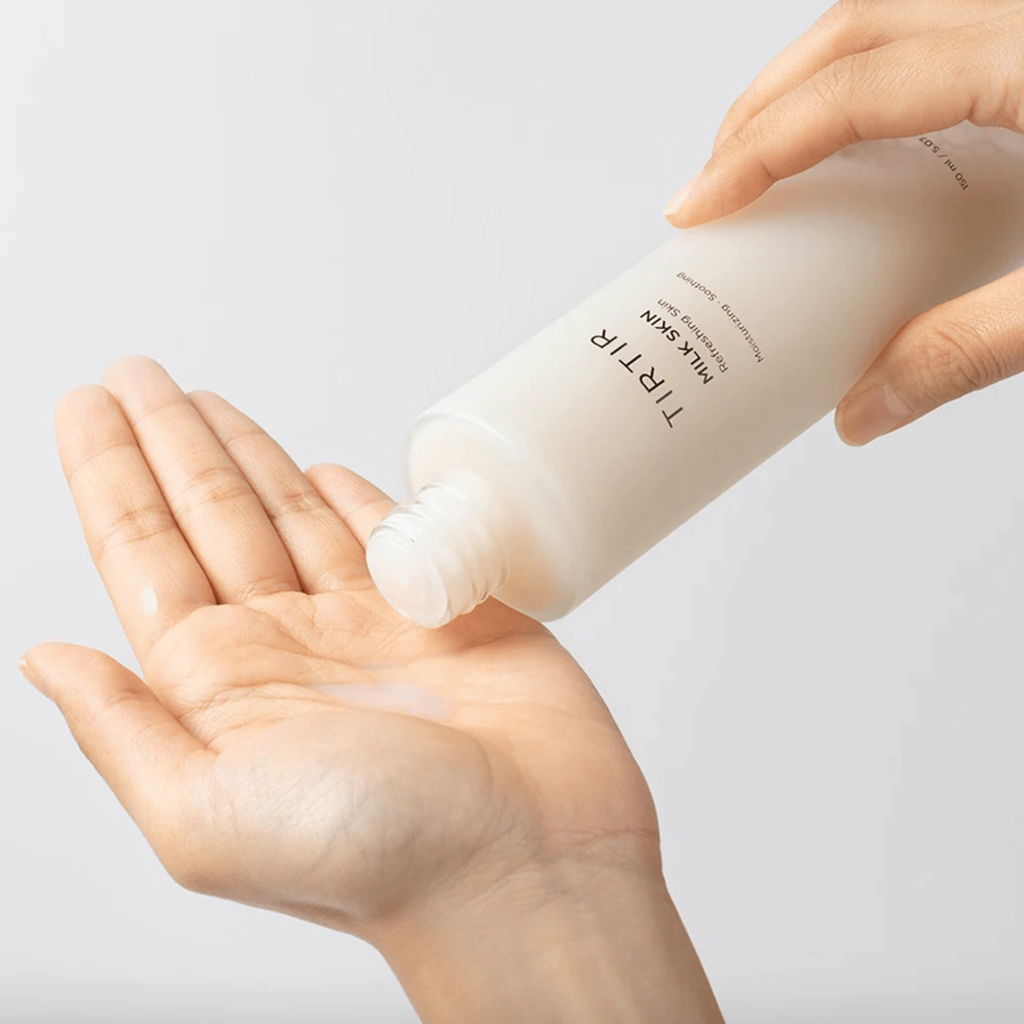 Zwei Hände halten die TIRTIR Milk Skin Toner Flasche vor beigem Hintergrund koreanische Hautpflege mit beruhigender Wirkung
