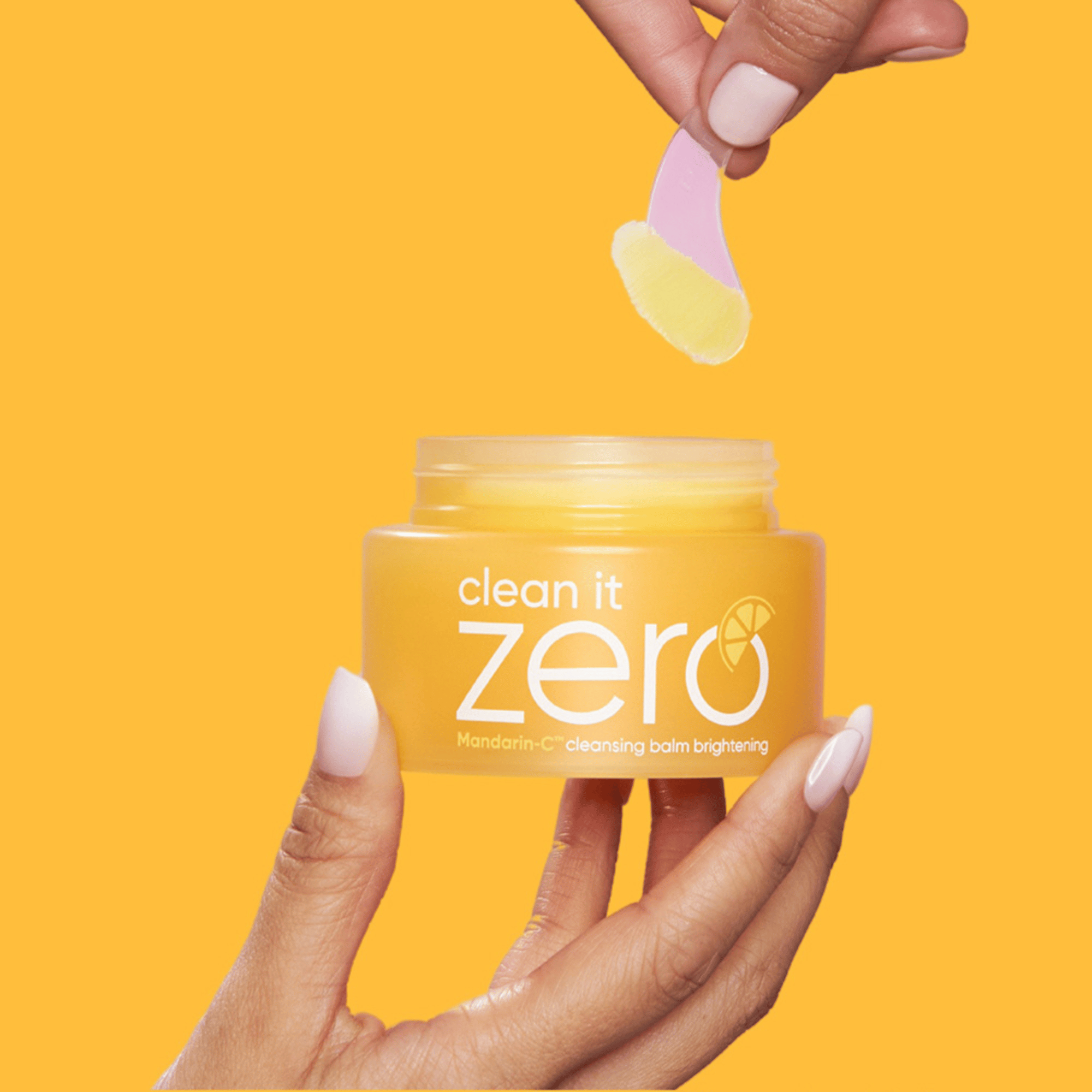 BANILA CO Clean It Zero Cleansing Balm Brightening 100ml mit Spatel – gelber Reinigungsbalsam auf orangem Hintergrund