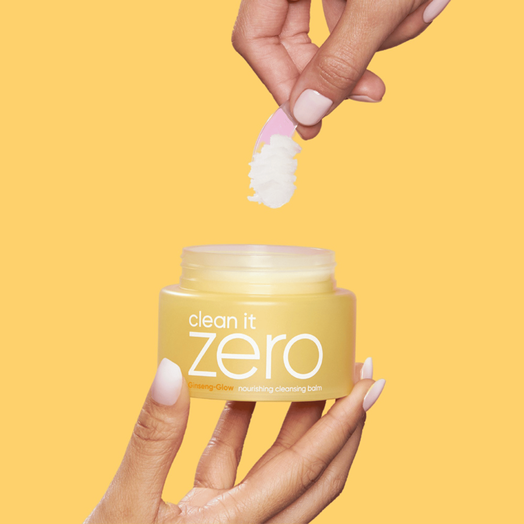 Gelbe Clean It Zero Nourishing Balm Dose wird mit Spatel entnommen, vor gelbem Hintergrund – K-Beauty Reinigungsbalsam