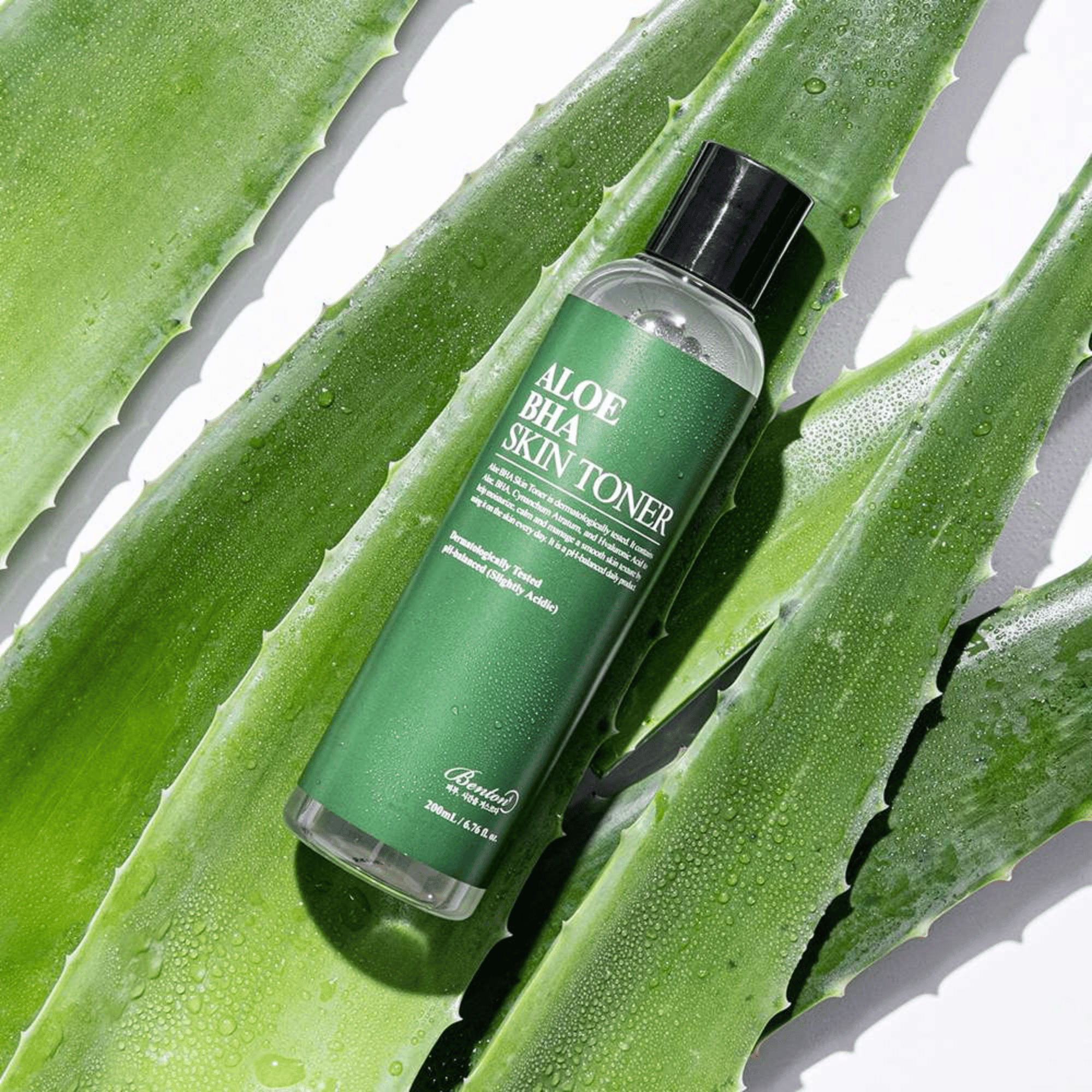 Eine Flasche Benton Aloe BHA Skin Toner 200 ml liegt auf einem frischen, taufrischen Aloe Vera Blatt Hintergrund.