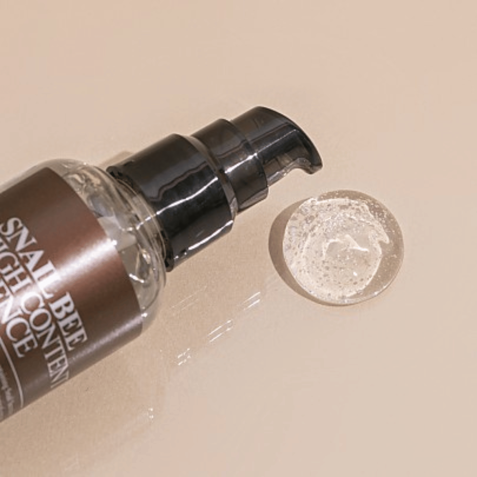 Die Pumpflasche der Benton Snail Bee High Content Essence gibt eine kleine Menge durchsichtiges Gel auf eine beige Oberfläche ab.