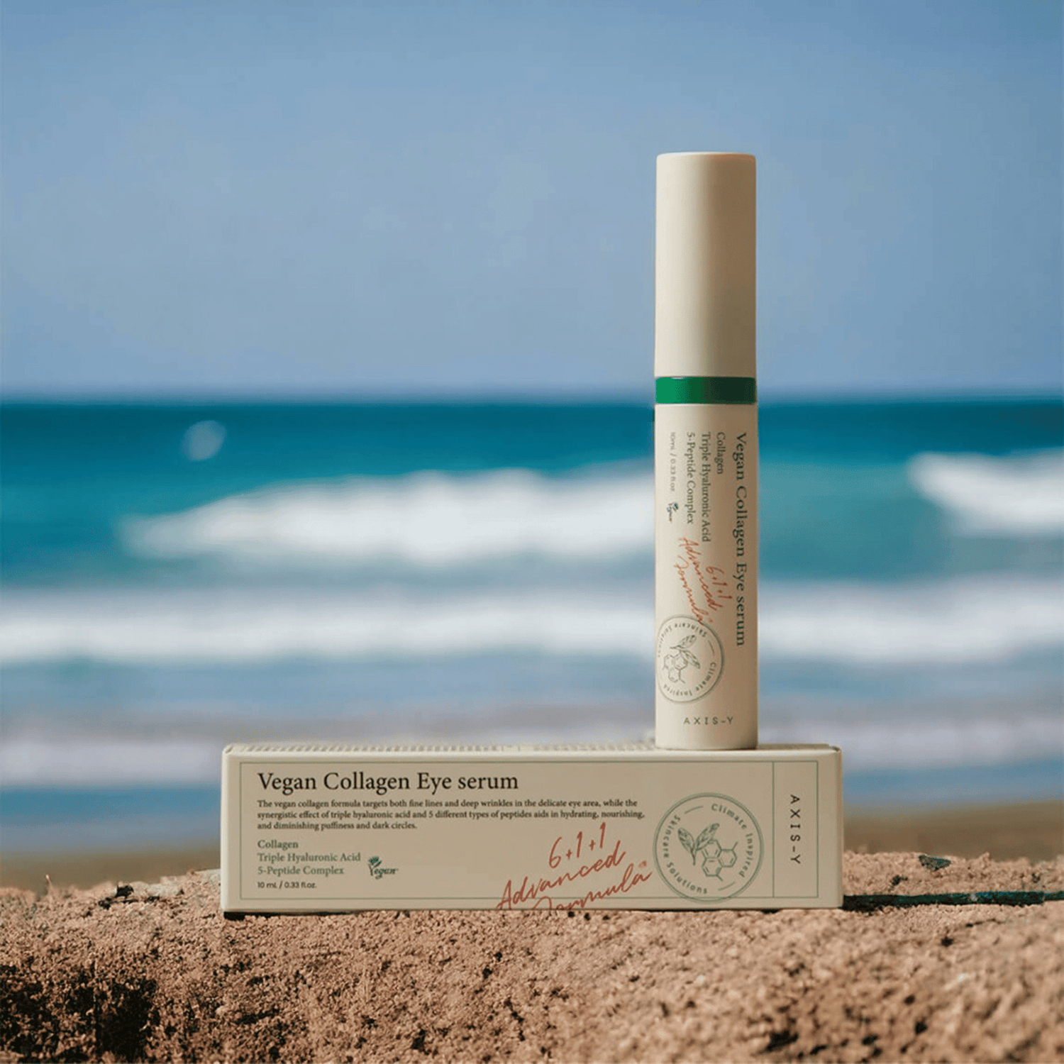 AXIS-Y Vegan Collagen Eye Serum stehend im Sand vor unscharfem Meereshintergrund, neben Umverpackung 