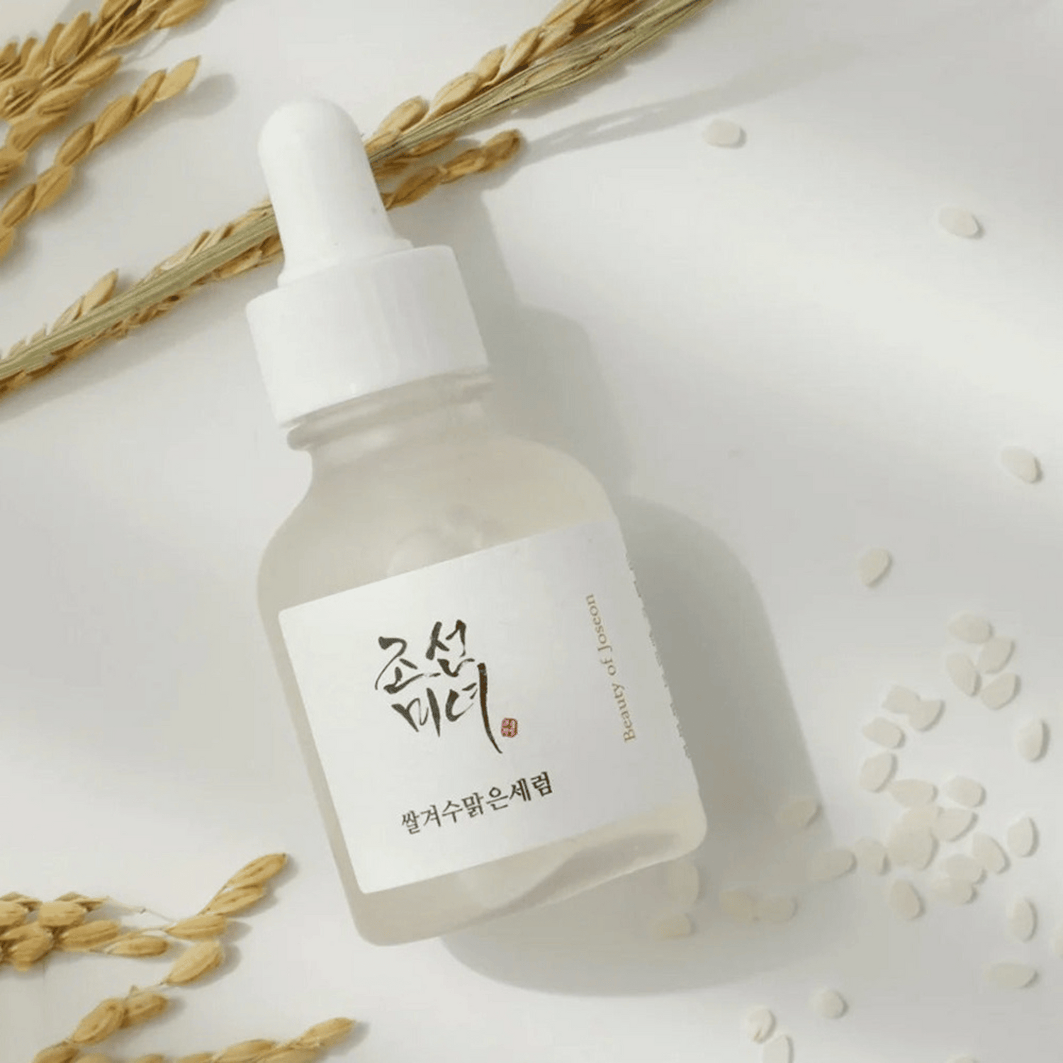 Serumflasche des Beauty of Joseon Rice + Alpha-Arbutin Glow Deep Serum mit Reiskörnern und Getreide auf weißem Hintergrund