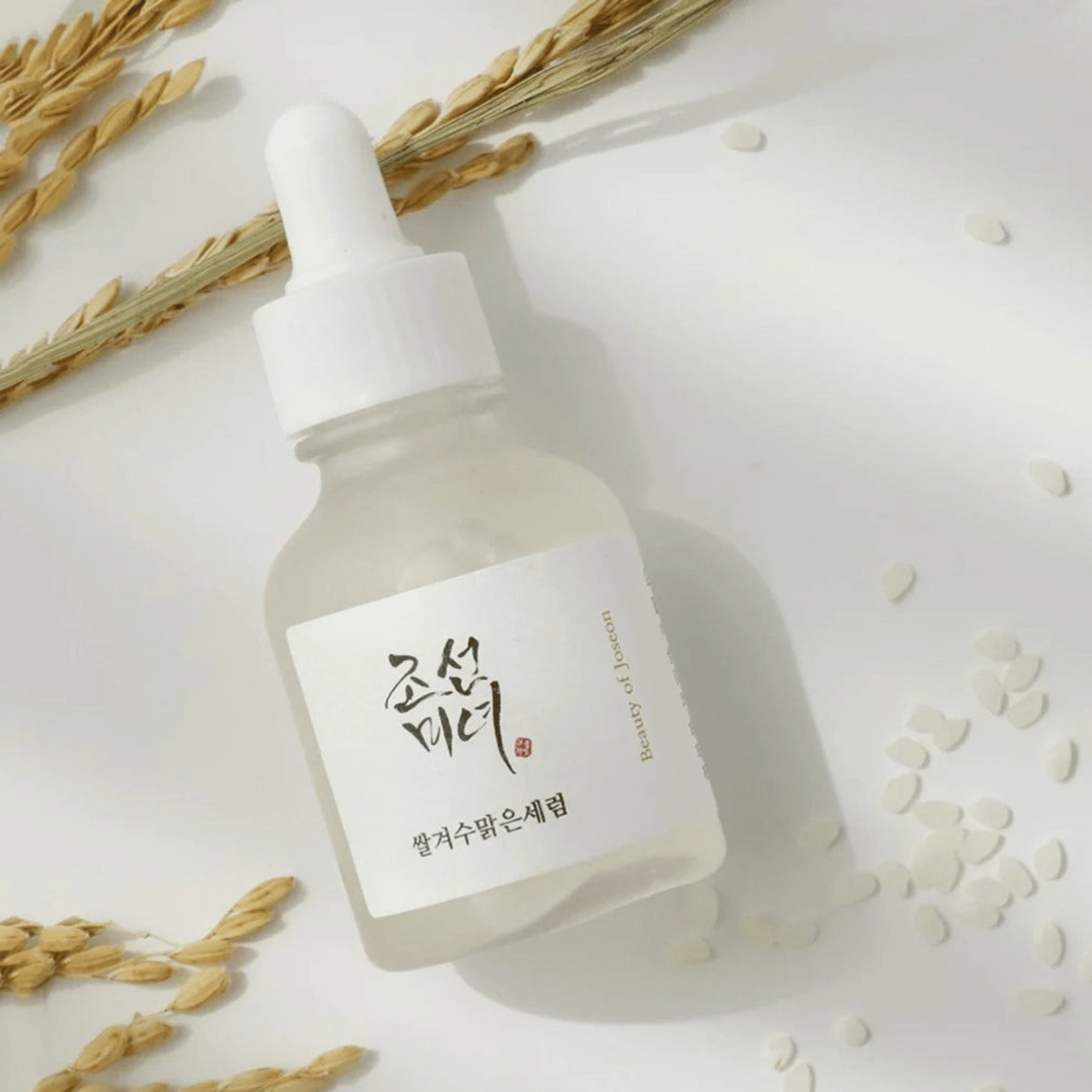 Serumflasche des Beauty of Joseon Rice + Alpha-Arbutin Glow Deep Serum mit Reiskörnern und Getreide auf weißem Hintergrund